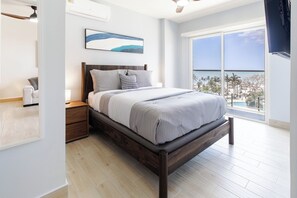 Ein Schlafzimmer mit Bett, Nachttisch und einem großen Fenster mit Blick.
