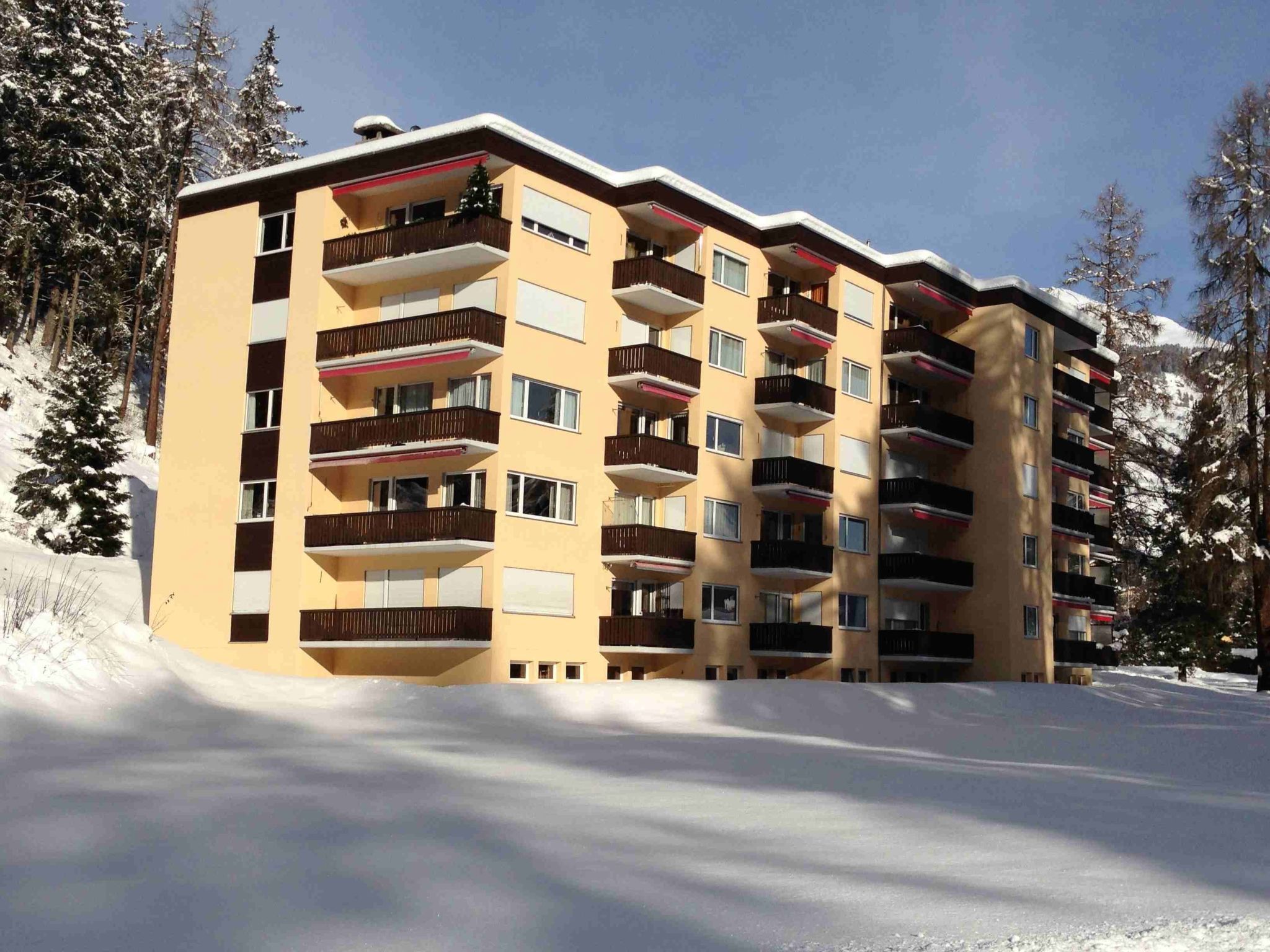 A multi-story building with balconies, surrounded by snow and trees.