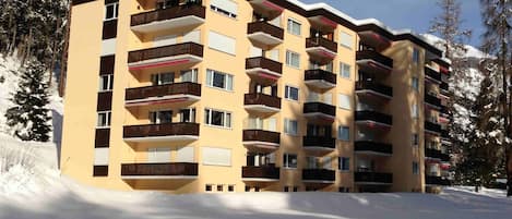 Un edificio de varios pisos con balcones, rodeado de nieve y árboles.