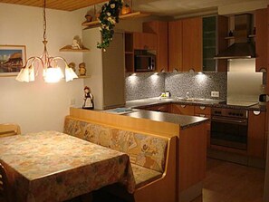 A kitchen with wooden cabinets, a built-in oven, and a dining area with a bench. - Brentsch Park, (Scuol) by Interhome (Scuol)