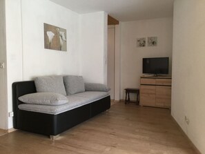 Ein modernes Wohnzimmer mit einem schwarzen Sofa, einem kleinen Holztisch und einem Fernseher auf einer Holzkommode.