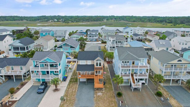 A coastal residential area with multi-story houses, a parking lot, and a view of the water and greenery in the distance. - 4 Bedroom, 4 Bathroom, Dunes Home, PET FRIENDLY (Supply)