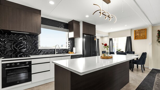 A modern kitchen with a central island, built-in oven, and dark cabinetry. - Spacious 5-Bedroom Family Home Near Lake Rotorua & Rotorua CBD (Rotorua)