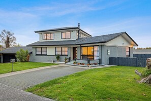 A two-story house with a garage, a front porch with potted plants, and a well-maintained lawn. - Spacious 5-Bedroom Family Home Near Lake Rotorua & Rotorua CBD (Rotorua)