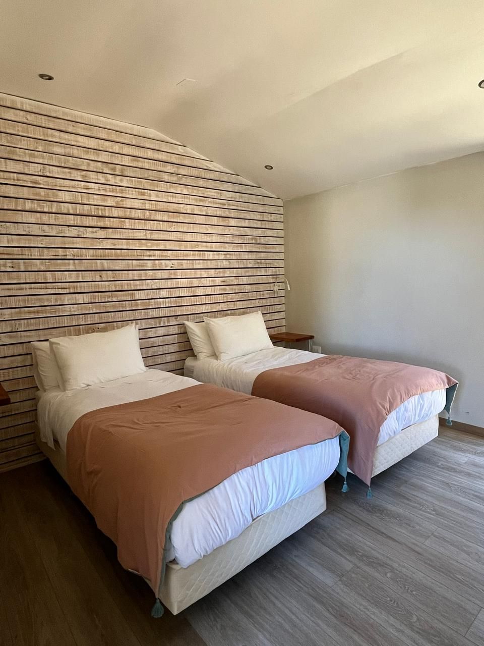 A bedroom with two beds, wooden headboard, and a wooden floor.