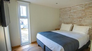 Un dormitorio con cama, cabecera de madera, televisor y puerta corrediza que da a un espacio exterior.