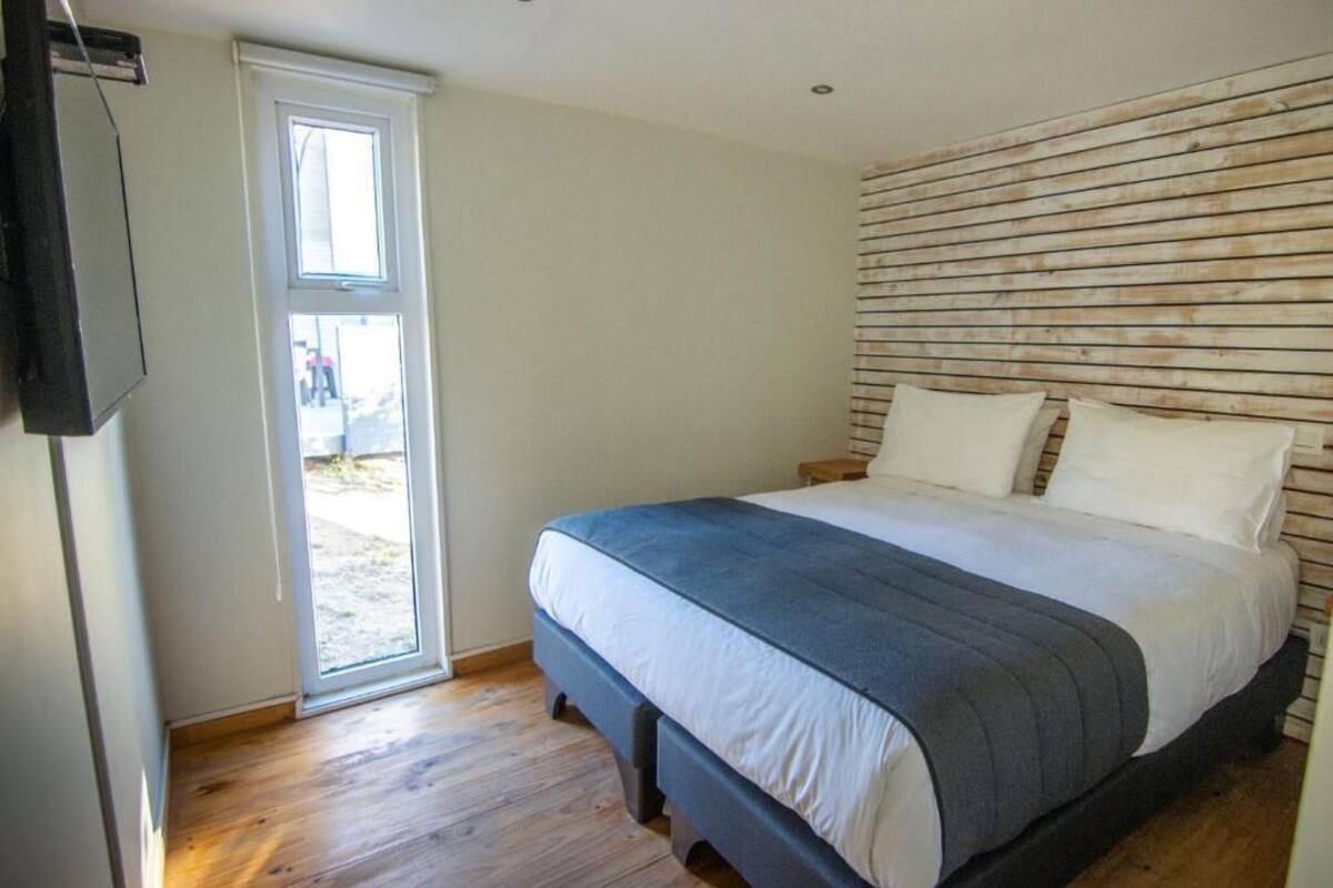 Un dormitorio con cama, cabecera de madera, televisor y puerta corrediza que da a un espacio exterior.