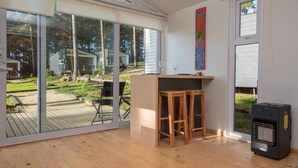 Una habitación con una puerta corrediza de vidrio que da a una terraza, una pequeña mesa de madera con taburetes y un calentador negro.