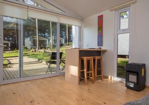 A room with a sliding glass door leading to a deck, a small wooden table with stools, and a black heater. - Curi Lodge Pichilemu (O'Higgins)