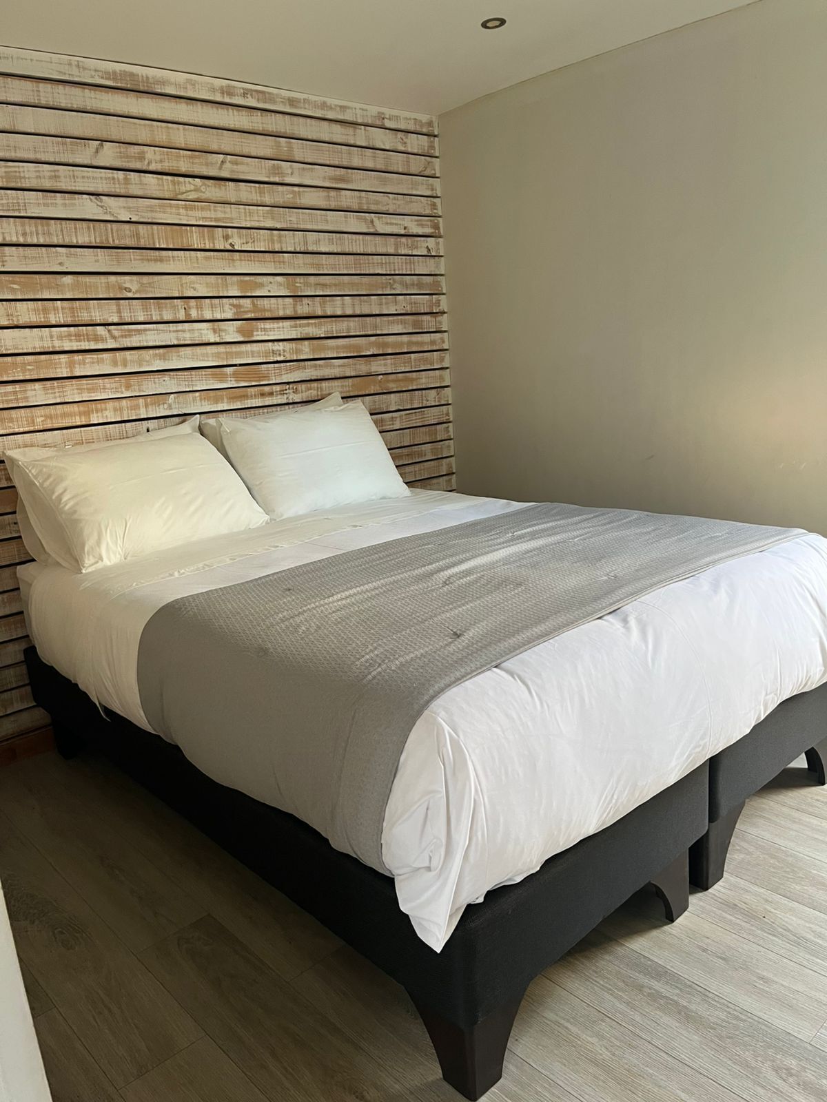 A bed with a wooden headboard, a grey bedspread, and white pillows.