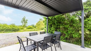 Un patio al aire libre cubierto con una mesa y sillas, rodeado de vegetación.