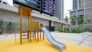 Un parque infantil con tobogán, estructuras de madera para escalar y suelo de goma amarillo.