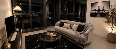 A modern living room with a sofa, a coffee table, a TV, and a large window with a city view.