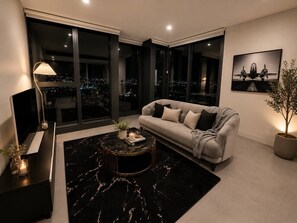 A modern living room with a sofa, a coffee table, and a large window offering a city view.