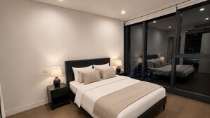 Une chambre moderne avec un grand lit, des tables de chevet et une vue sur l’extérieur grâce à une porte vitrée.