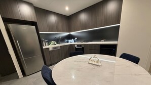 Une cuisine moderne avec des meubles en bois foncé, un réfrigérateur en acier inoxydable, une table ronde en marbre et un panneau indiquant : « Soyez gentils ».
