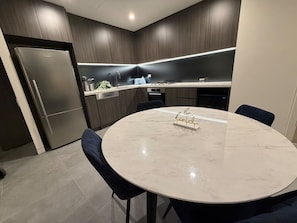 Eine moderne Küche mit dunklen Holzschränken, einem Edelstahlkühlschrank, einem runden Marmortisch und einem Schild mit der Aufschrift 'be kind'.