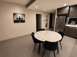 A modern kitchen with dark wood cabinets, a stainless steel refrigerator, and a round marble table with chairs. - Luxurious City View near Accor Stadium (Lidcombe)