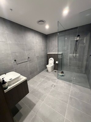 A modern bathroom with a glass-enclosed shower, a white toilet, and a marble sink. - Luxurious City View near Accor Stadium (Lidcombe)
