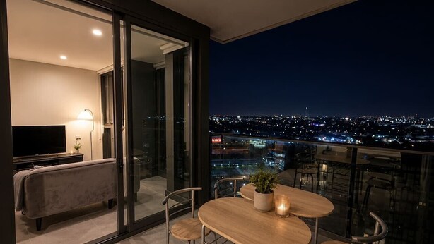 Un balcon avec une table, des chaises, une plante et un téléviseur dans la pièce adjacente.