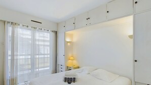 Hotellihuone, jossa on suuri sänky, yöpöytä lampun kanssa ja ikkunasta avautuva näkymä, jonka edessä on läpikuultavat verhot.