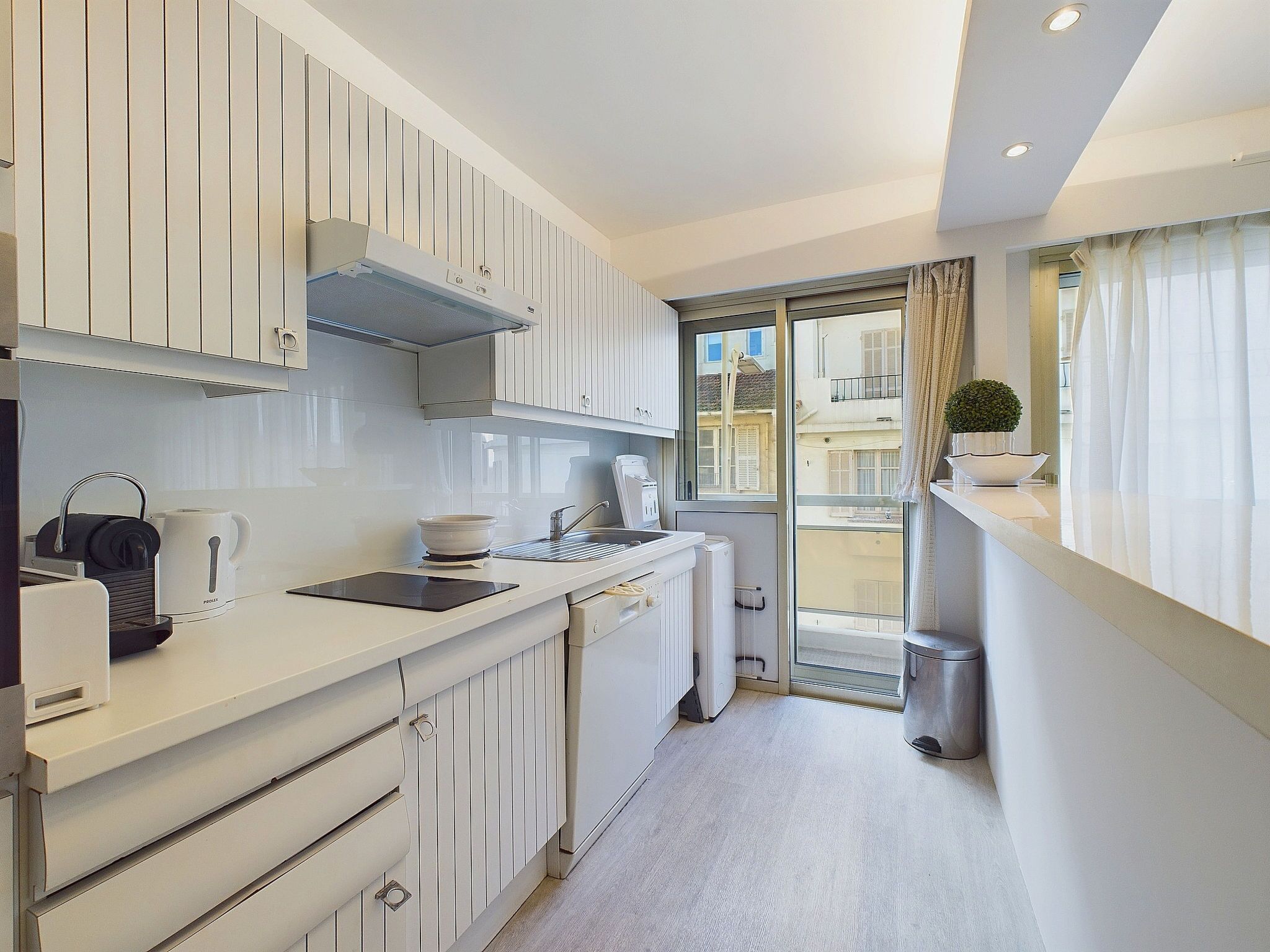 A modern kitchen with white cabinetry, a built-in oven, and a window overlooking a balcony.