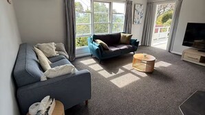 A modern living room with a sofa, a coffee table, and a TV. - Welcome to Blue Haven in St John’s - incl pets (Whanganui)