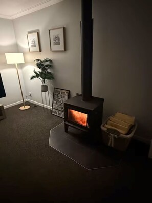 A cozy room with a wood-burning stove, a floor lamp, and framed pictures on the wall.
