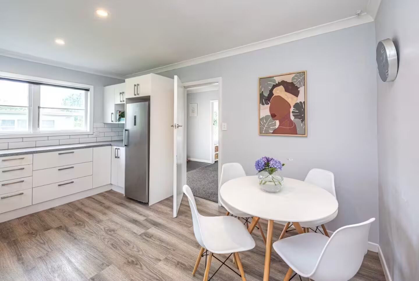 A modern kitchen with white cabinets, a stainless steel refrigerator, and a dining area with a round table and white chairs.. Welcome to Blue Haven in St John’s - incl pets
