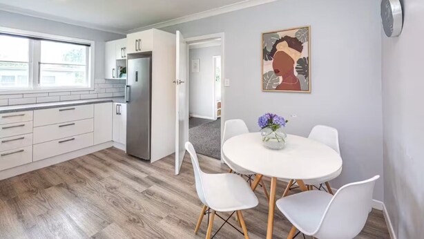 A modern kitchen with white cabinets, a stainless steel refrigerator, and a dining area with a round table and white chairs. - Welcome to Blue Haven in St John’s - incl pets (Whanganui)