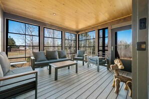Ein überdachter Außenbereich mit Holzterrasse, großen Fenstern und Blick ins Freie.
