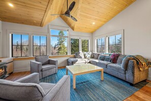 Ein modernes Wohnzimmer mit Kamin, grauen Sofas, einem Couchtisch und großen Fenstern.