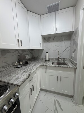 A kitchen with white cabinets, a marble countertop, a sink, and a stove. - Elegant apartment in an excellent neighborhood (Port St. Lucie)