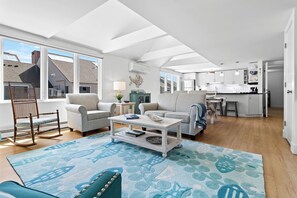A spacious living area with a high ceiling, a dining table, and a kitchen in the background.