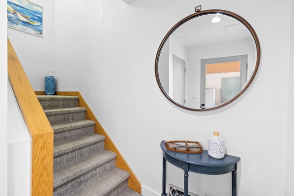 Un escalier avec des rampes en bois, un miroir rond accrochĂ© au mur et une petite console ornĂ©e dâobjets dĂ©coratifs.