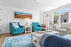 A living room with teal armchairs, a white coffee table, a fireplace, and a large window.