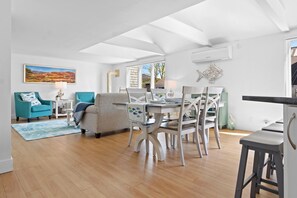 A spacious living area with a dining table, chairs, a sofa, and a painting on the wall.