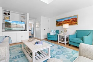 A modern living room with a flat-screen TV, teal armchairs, a coffee table, and a painting on the wall.