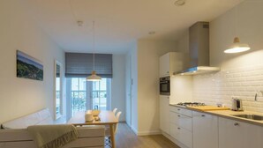 Une cuisine moderne avec des meubles blancs, une cuisinière à gaz et un coin repas comprenant une table et des chaises.