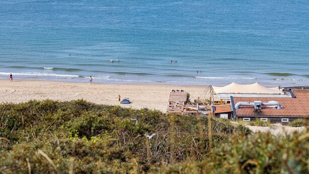 Une plage avec un rivage sablonneux, quelques personnes et un bâtiment avec un toit rouge, visible au premier plan.