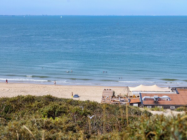 A beach with a sandy shore, a few people, and a building with a red roof in the foreground. - Duingolf a by Interhome (Koudekerke)