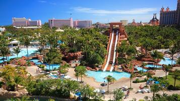 A resort with multiple swimming pools, palm trees, and a large water slide.