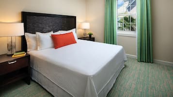 A neatly made bed with white and red pillows, a dark headboard, and a nightstand with a lamp and a book.