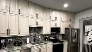 Una cucina moderna con mobili bianchi, elettrodomestici in acciaio inossidabile e una parete di fondo in marmo.