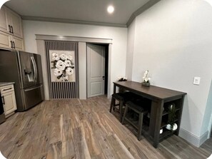 A kitchen with a dark wooden table, a refrigerator, and a door with a floral design. - Cozy, fully furnished 2-bedroom house in lovely Comfort with AC and game room. (Comfort)