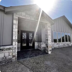 A building with a stone facade, a black door with decorative glass panels, and a clear sky. - Cozy, fully furnished 2-bedroom house in lovely Comfort with AC and game room. (Comfort)