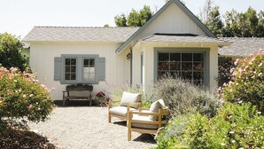 Una casa con vialetto sterrato, una panchina in legno e un giardino con diverse piante e fiori.