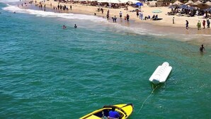 Een strand met een rij hotels, helderblauw water en een gele boot.