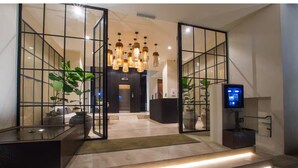 Een moderne lobby met een glazen scheidingswand, een receptiebalie, een televisie en een trap naar de bovenverdieping.