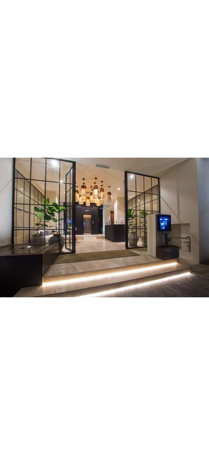 Eine moderne Lobby mit Glastrennwand, einer Rezeption, einem Fernseher und einer Treppe zum Obergeschoss.